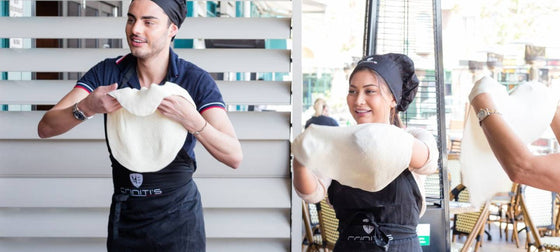 Two people flipping a pizza dough