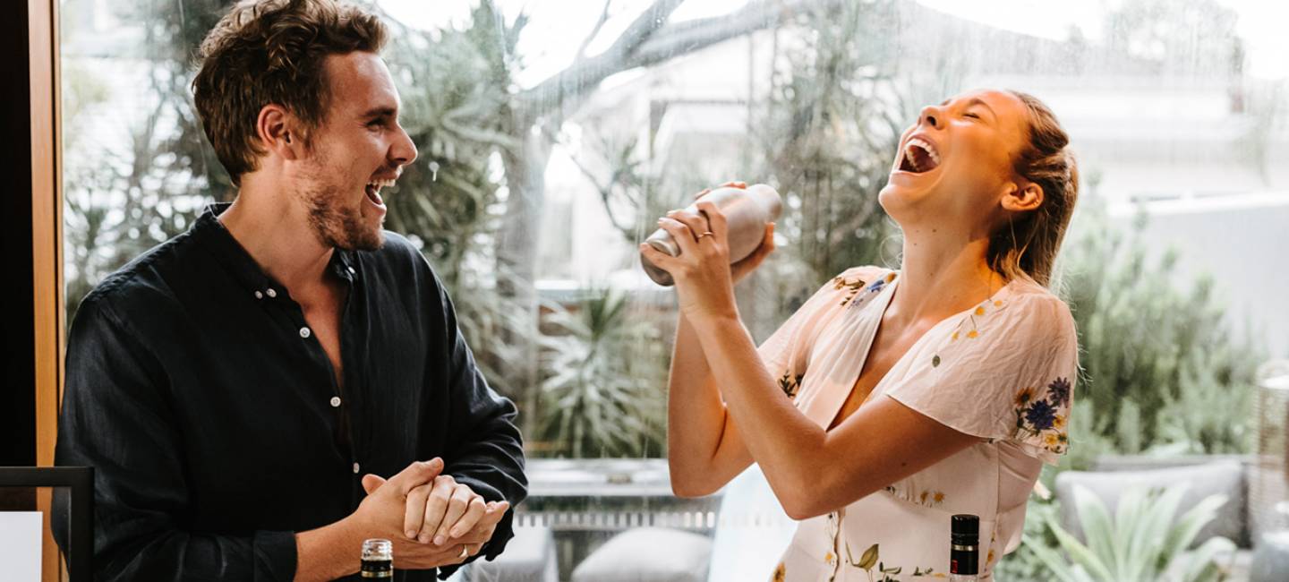 Two people laughing and a woman shaking a cocktail. 