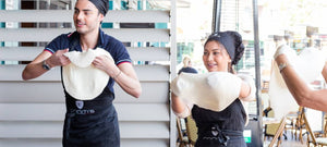 Two people flipping a pizza dough